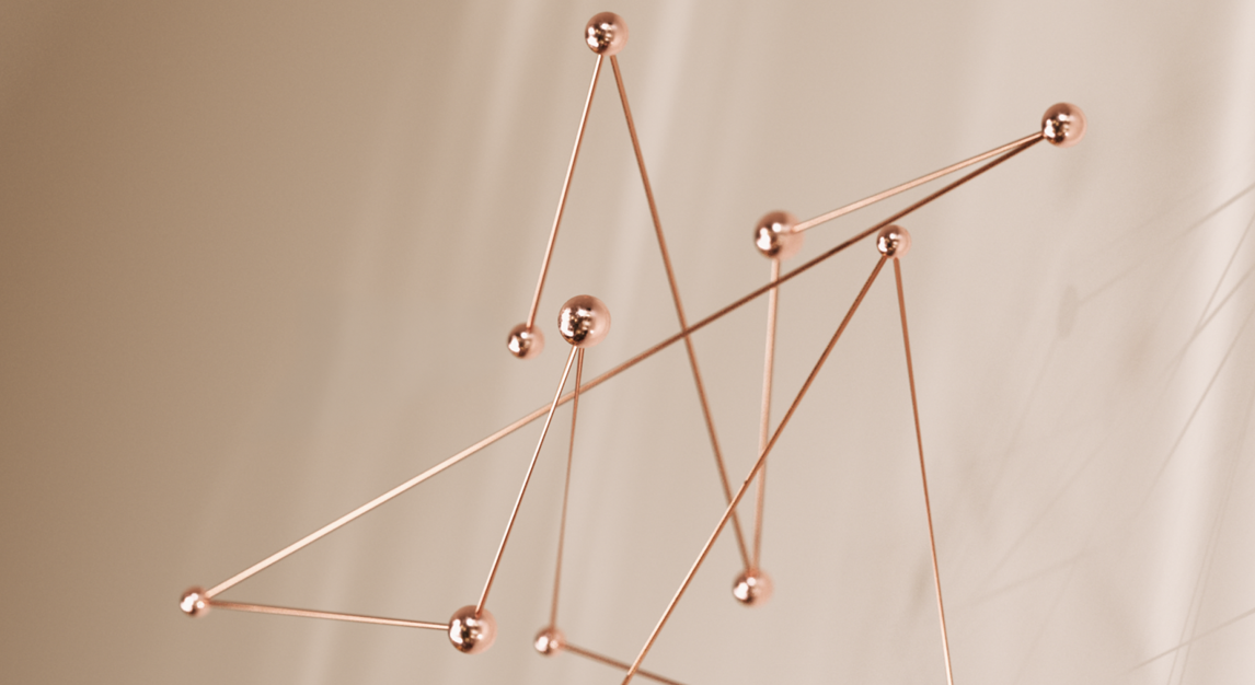 A delicate copper wire and sphere kinetic sculpture suspended against a warm beige backdrop